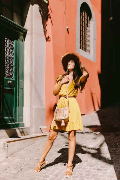 穿着夏装 头戴草帽 头戴手提包走路的漂亮女人 穿着黄色夏装 头戴粗纱帽 头戴草袋的黑发长发女子在老城区街道上行走的画像 — 图库照片