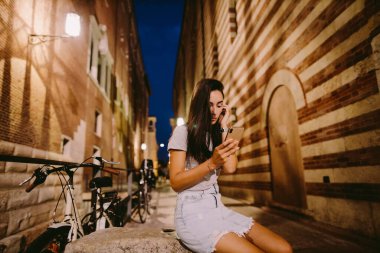 Akşamları açık havada akıllı telefon kullanan bir kadın. Avrupa, İtalya ve Verona 'da akıllı telefonlu bir kadın sokakta oturuyor..