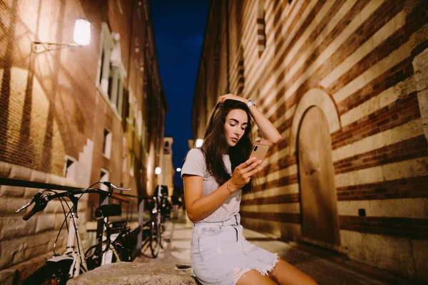屋外でスマホを使っている女性です ヨーロッパ イタリア ヴェローナのスマートフォンで通りに座っている女性 — ストック写真