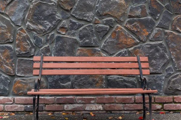 Lavička v parku proti kamenné zdi — Stock fotografie