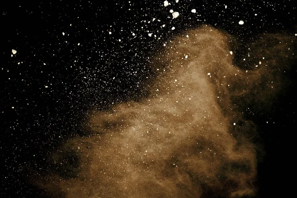 Explosion of brown powder on black background.