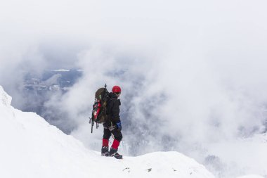 Erkek bir dağcı dağın kış yamacında durur ve uzaklığa bakar..