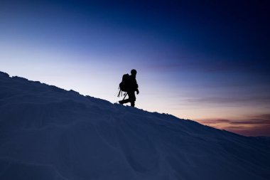 Gün batımında bir adam dağın tepesinden iner, karın dokusu görünür.