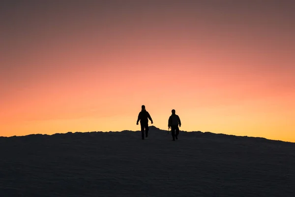 Two silhouettes men after climbing a mountain descend from the mountain at sunset