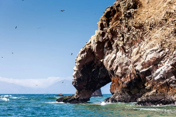 Een rots met een grot met uitzicht op de zee, meeuwen vliegen rond, bergen, Ballestas eilanden zijn zichtbaar in de verte, Paracas reserv, Peru, Latijns-Amerika. — Stockfoto