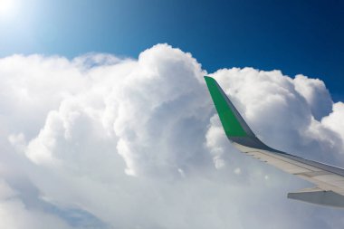 Bir uçağın penceresinden bak, beyaz bulutlar, mavi gökyüzü, bir uçağın kanadı. Ray sol üst köşede..