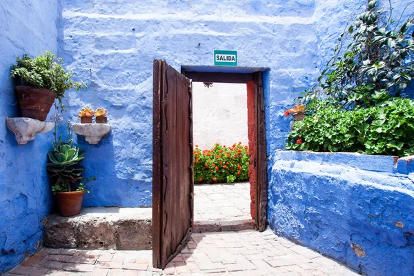 Courtyard with blue walls, an open wooden door in the center, flower pots along the walls, monastery Santa Catalina, Arequipa, Peru.