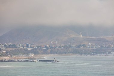 2019-12-07 Lima Peru. City view, in the foreground the ocean, lighthouse, statue, mountains, fog.