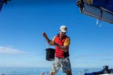 Bir adam güverteyi yıkamak için kovayla denizden su çeker.