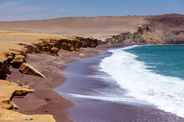 Kayalık kayalıklar, kızıl kumlu plaj, okyanus dalgaları manzarası. Paracas Ulusal Rezervi.