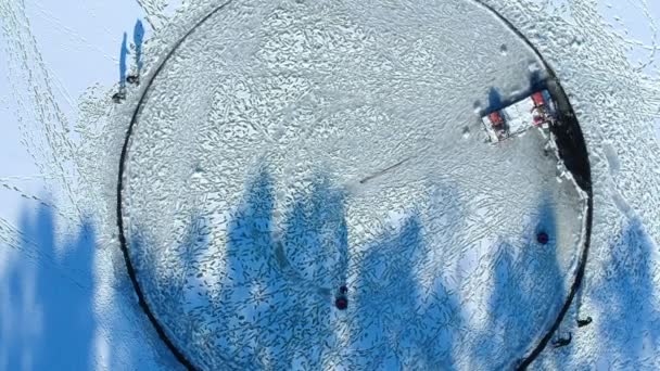 Top view of a huge carved round hole. A connected motor makes it spin. People ride on a large ice floe. Long shadows. — Stock Video