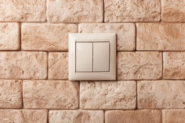 Light switch on a beige brick wall.