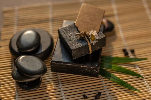 charcoal coal carbon black soap bar on a raw wood bamboo background lava stone spa skin care hygiene concept. black black stone backgroun. raw wood background lava stone spa skin care hygiene concept