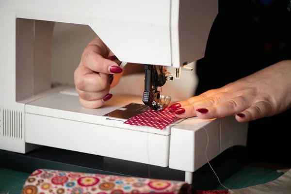 detail of womans hands sewing maching Seamstress sews clothes made of red cloth on a sewing machine. Work by the light of the built-in hardware lamp. Steel needle with looper and presser foot close-up