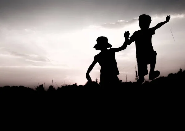 Kinderen springen van een rots bij zonsondergang, silhouetten — Stockfoto