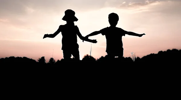 Silhouetten von Kindern, die bei Sonnenuntergang von einer Klippe springen — Stockfoto