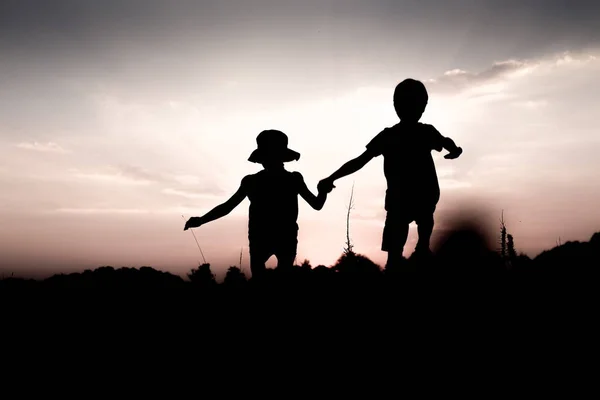 Los niños saltan de una colina tomados de la mano al atardecer — Foto de Stock