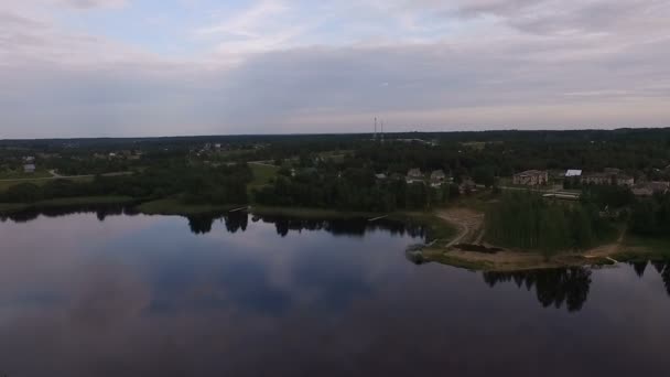 En vy från luften till en liten lugn sjö. Sommar, gröna stränder, moln återspeglas. På den bortersta stranden är små hus — Stockvideo