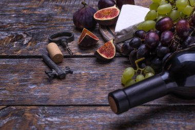 Kırmızı şarap bir şişe, mantar bottlescrew ve ürünler - peynir, üzüm, fındık, zeytin, incir ahşap bir gemide bir dizi arka plan