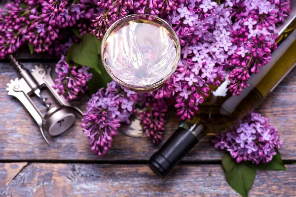 White  wine in a glass and a bottle with lilac flowers on a wooden board, background. Top view. — Stock Photo, Image