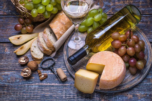 White wine in a bottle, cork bottles crew and a set of products - cheese, grapes, nuts, olives, figs on a wooden background.