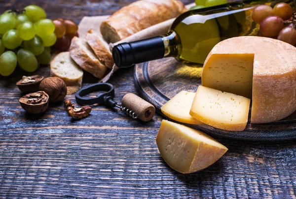 White wine in a bottle, cork, bottle screw and a set of products - cheese, grapes, nuts, olives, figs on a wooden board, background