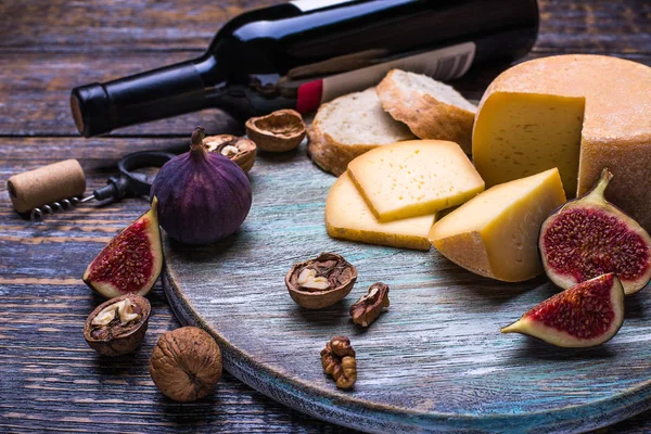 Red wine in a bottle, cork, bottle screw and a set of products - cheese, grapes, nuts, olives, figs on a wooden board, background