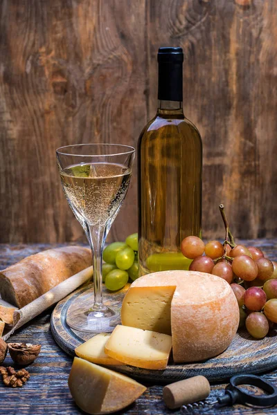 El vino blanco en la botella, el corcho, el tornillo de botella y el juego de los productos - el queso, las uvas, las nueces, las aceitunas, los higos sobre la tabla de madera, el fondo —  Fotos de Stock