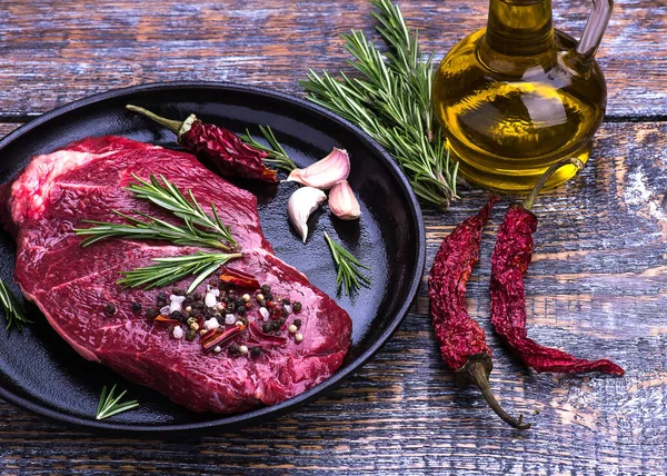 Ham sığır eti biftek, tuz, biber, sarımsak, biberiye, ahşap masa, arka plan üzerinde siyah tava.
