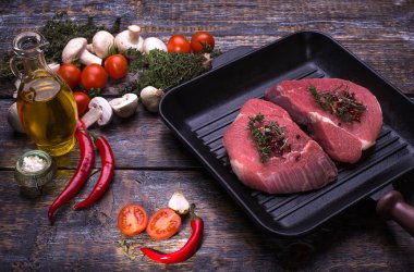 Ham sığır eti biftek, siyah pan, tuz, biber, sarımsak, biberiye ahşap gemide, arka plan.