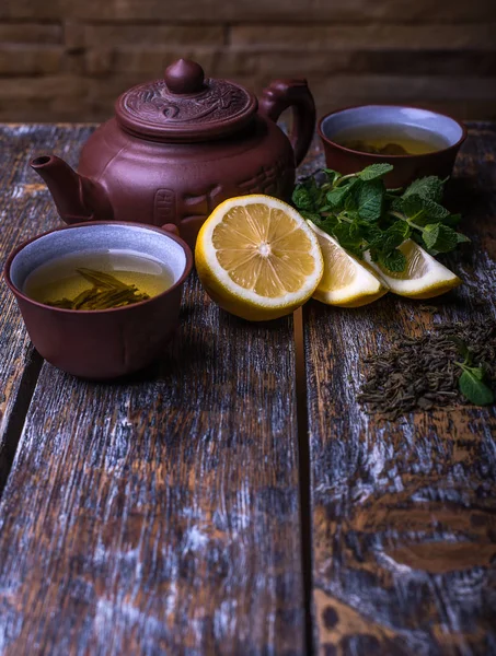 Thé vert dans la théière avec des feuilles de citron et de menthe sur fond de bois — Photo