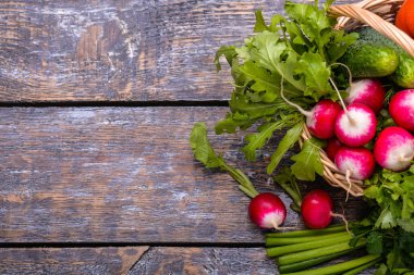 Hasat sebzeler: sadishes, domates, salatalık, maydanoz, soğan, roka, sepeti ahşap arka plan üzerinde