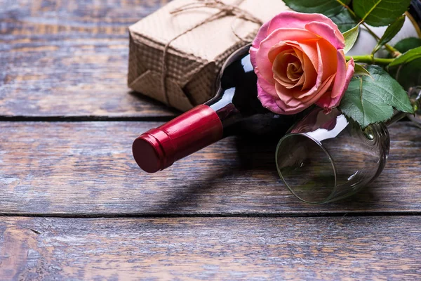 Red wine bottle, present box. wine glass and flowers roses on wooden background