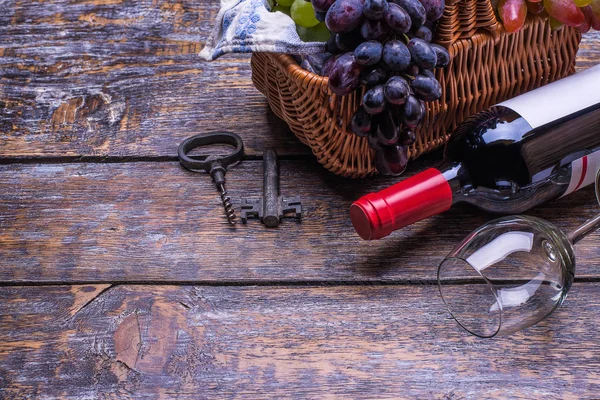 Red wine bottle, wine glass, cork, bottle screw set of products -  grapes at the basket on a wooden board, background