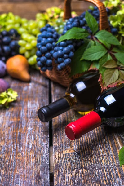 White wine bottle, red wine  bottle, cork, bottle screw and a set of products -  grapes, nuts, plums, pears, autumn foliage  on a wooden board, background