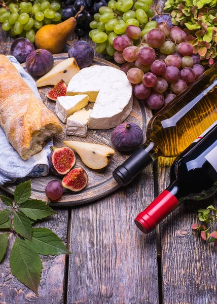 Red wine in a bottle and white wine bottle, cork, bottle screw and a set of products - cheese, grapes, nuts, pears, plums, flowers, figs, white bread, baguette on a wooden board, background