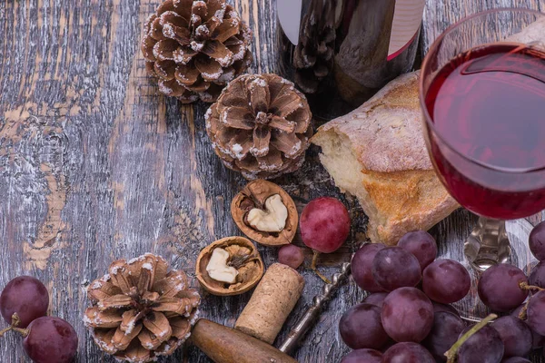Red wine bottle, red wine  glass, cork, bottle screw and a set of products -  grapes, nuts, bread, cones  on a wooden board, background