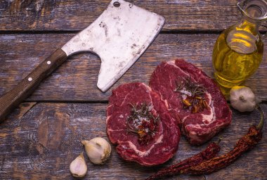 Ham sığır eti, ızgara biftek, tuz, acı biber, sarımsak, domates, kekik, biberiye ahşap bir masa, arka plan üzerinde.