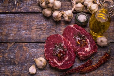 Ham sığır eti, ızgara biftek, tuz, acı biber, sarımsak, domates, kekik, biberiye ahşap bir masa, arka plan üzerinde.