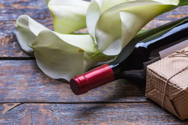 Red wine bottle, present box and flowers roses on wooden background