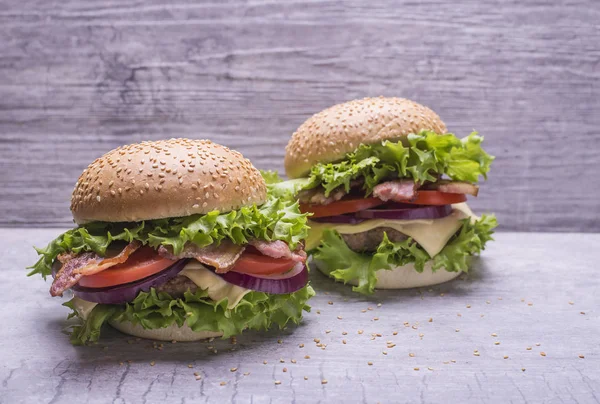 Hausgemachter Burger mit Rinderschnitzel, frischem Gemüsesalat, Tomaten, Zwiebeln, Käse, Ketchup, Semmel mit Sesam auf grauem Hintergrund. — Stockfoto