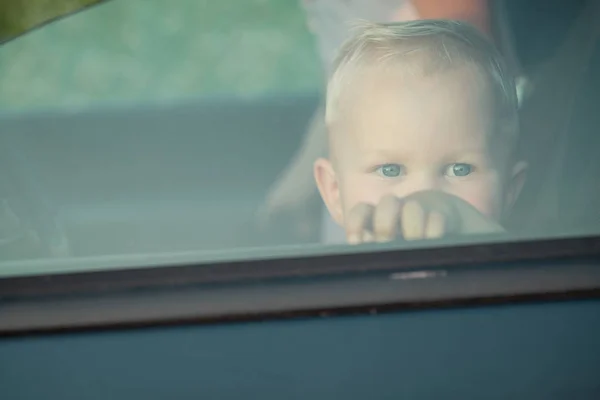 Un niño pequeño sentado en el coche y mirar hacia fuera desde el coche ganar —  Fotos de Stock