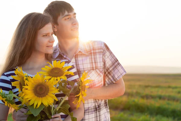 Retrato de pareja joven de pie con girasoles en un campo . —  Fotos de Stock