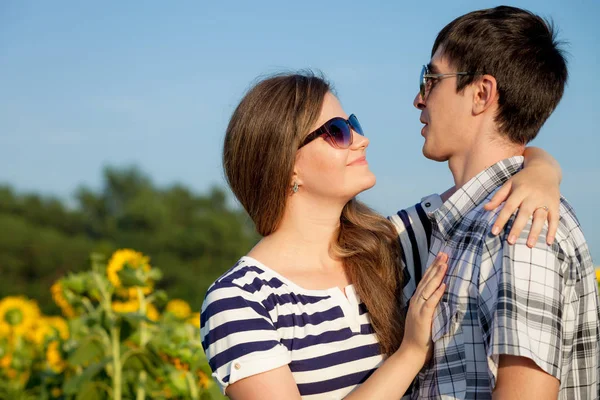 Porträt eines jungen Paares, das mit Sonnenblumen auf einem Feld steht. — Stockfoto