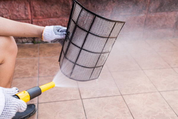 Person spraying water onto air conditioner filter to clean dust