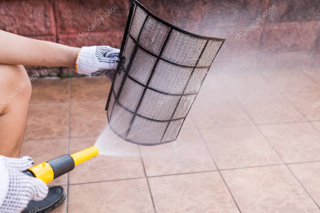 Person spraying water onto air conditioner filter to clean dust — Stock