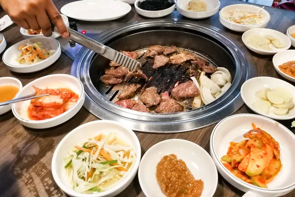 Pessoa churrasco carne no poço bbq durante conjunto de refeição coreana — Fotografia de Stock