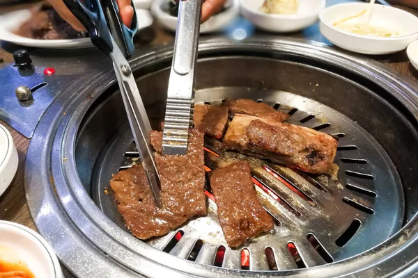 Pessoa churrasco carne no poço bbq durante conjunto de refeição coreana — Fotografia de Stock