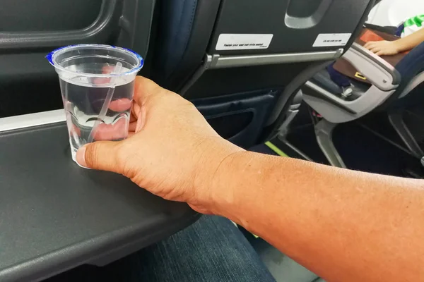 Ręka trzyma jednorazowe wody mineralnej na stole w powietrze samolot — Zdjęcie stockowe