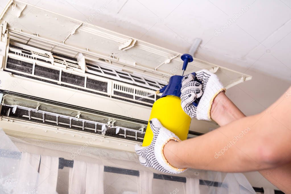 Technician spraying chemical water onto air conditioner grid to 